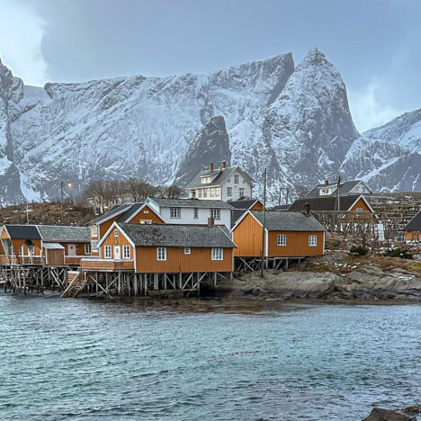 Isole Lofoten, scorcio villaggio di pesatori con case gialle e sullo sfondo montagne innevate