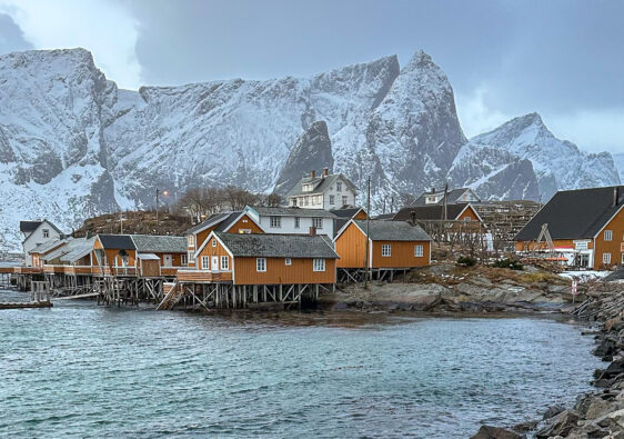 Isole Lofoten, scorcio villaggio di pesatori con case gialle e sullo sfondo montagne innevate